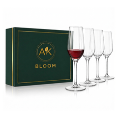 AK BLOOM set of 4 clear stemmed wine glasses, one partially filled with red wine, displayed beside a dark green gift box with gold trim.